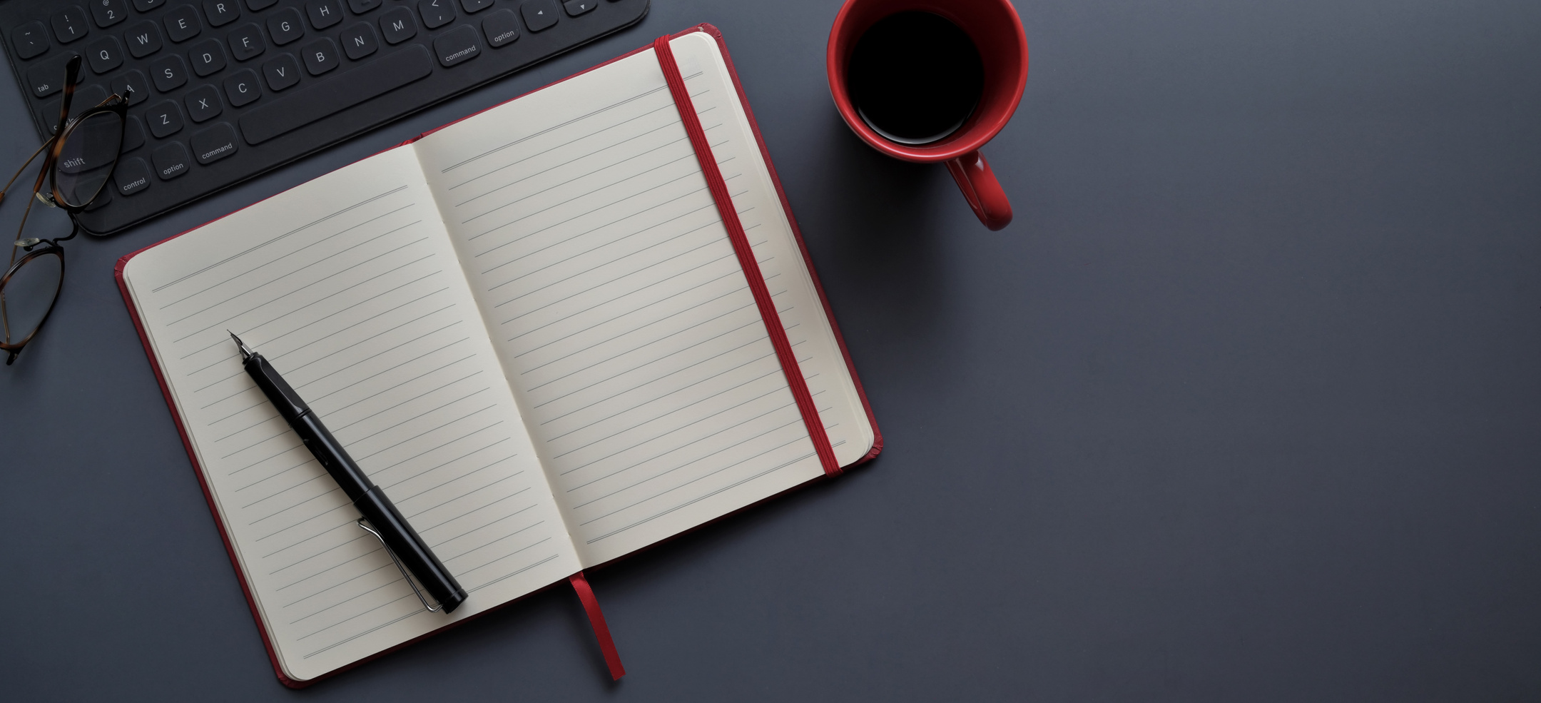 Notebook and Pen Beside Red Mug on Gray Surface
